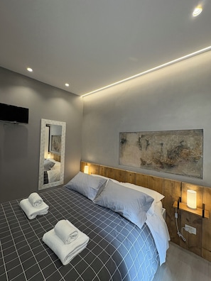 A modern hotel room with a large bed, a flat-screen TV mounted on the wall, and a painting above the bed. - Catullo 12 (Verona)