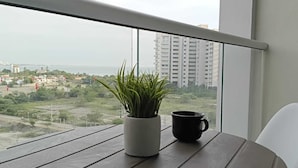 Ein Balkon mit Topfpflanze und Tasse, mit Blick auf eine Stadtlandschaft mit Gebäuden und Grünflächen.