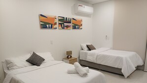 Ein Hotelzimmer mit zwei Betten, weißer Bettwäsche, einem kleinen Nachttisch mit Lampe und drei abstrakten Bildern an der Wand.