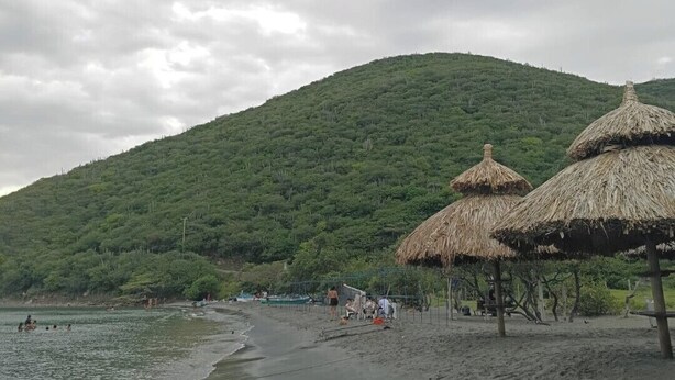 Ein Strand mit Reetdachschirmen und einem Berg im Hintergrund.