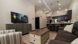 A modern living room with a flat-screen TV, a sofa, a coffee table, and a kitchen area with a bar. - Sears Lofts | The Voedsch (Aberdeen)