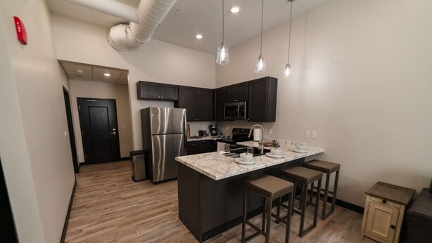 A modern kitchen with dark cabinetry, stainless steel appliances, and a marble countertop. - Sears Lofts | The Voedsch (Aberdeen)