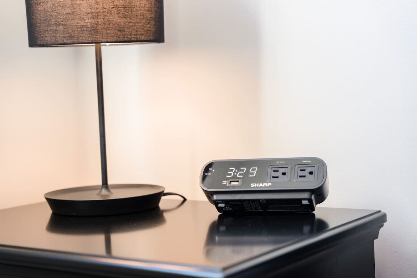A black digital clock with a USB port and a power outlet on a wooden nightstand.