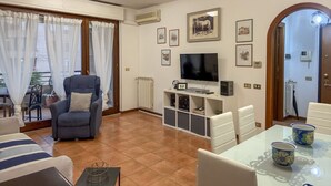 Una sala de estar con televisor, sofá, sillón y una mesa de comedor con tazas.