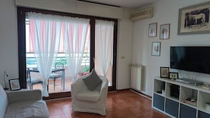 Ein Wohnzimmer mit Sofa, Sessel, Fernseher und Heizkörper.