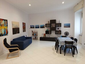 Un salon moderne avec un canapé bleu, une table à manger avec des chaises et une étagère noire agrémentée d’objets décoratifs.