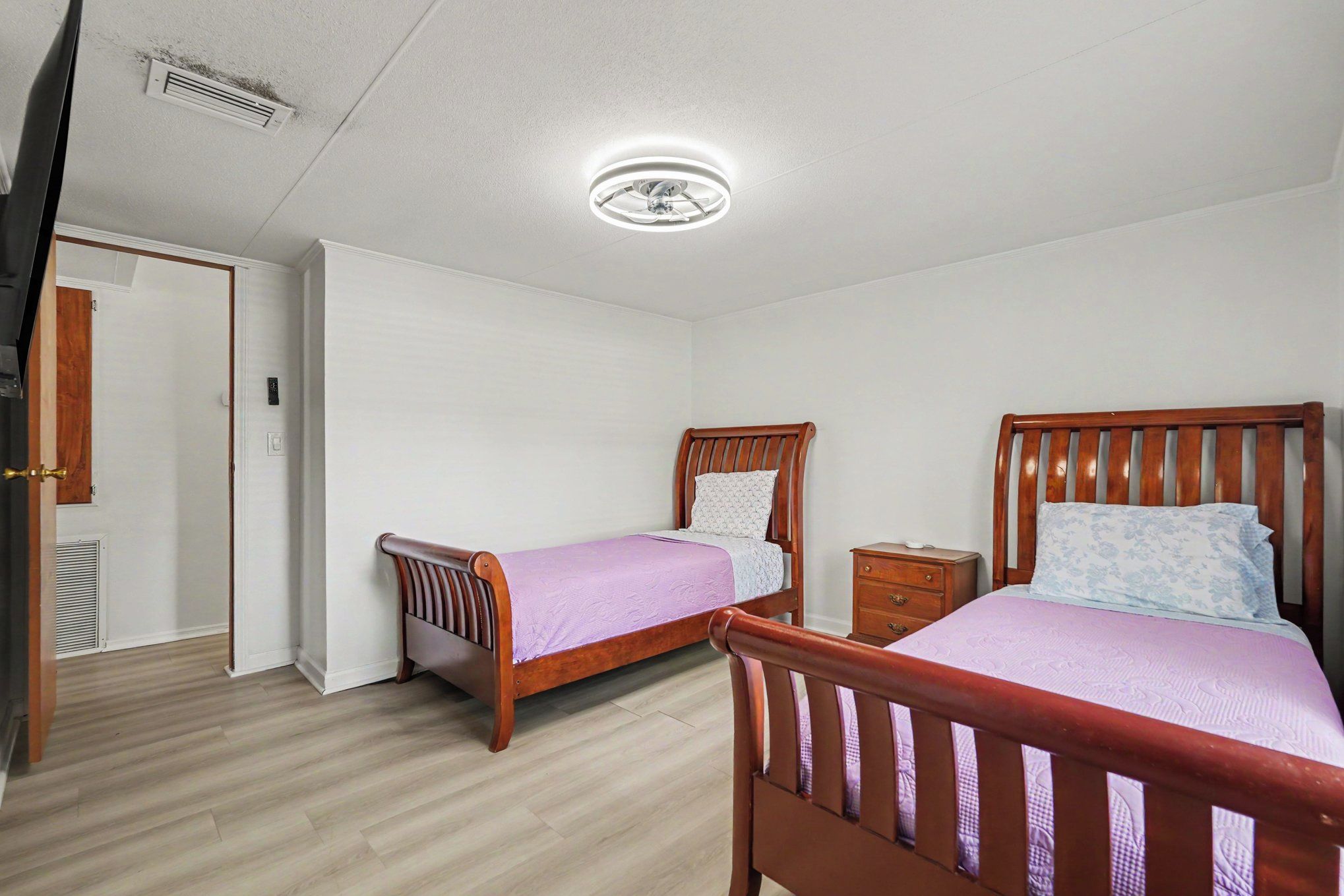 Un dormitorio con dos camas de madera, una mesita de noche, una puerta y una lámpara en el techo.