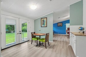 Un comedor con mesa y sillas, una cocina con armarios y vistas a un espacio exterior verde a través de un ventanal.