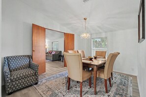 Un comedor con mesa de madera y seis sillas, un sillón estampado y una araña.