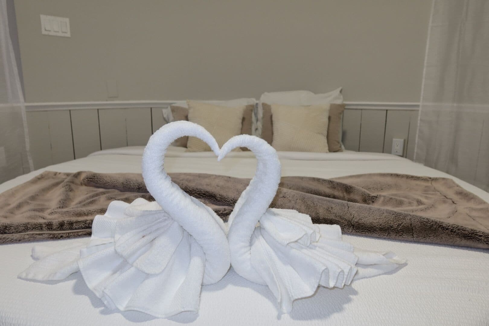 A bed with a heart-shaped towel arrangement and a brown blanket.