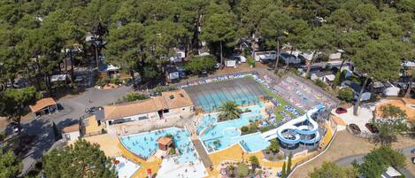 An aerial view of a resort with a large swimming pool, a water slide, and multiple beach areas.