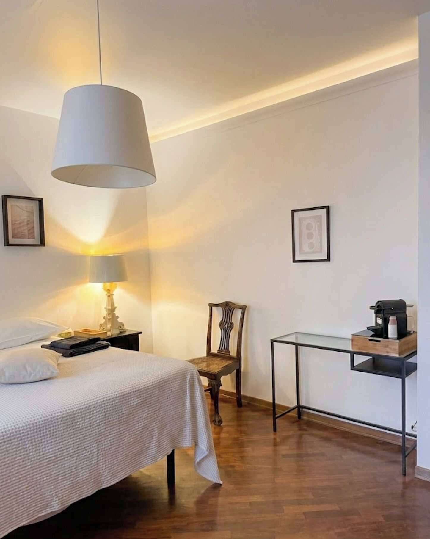 A bedroom with a bed, a chair, a small table with a coffee maker, and a hanging lamp.