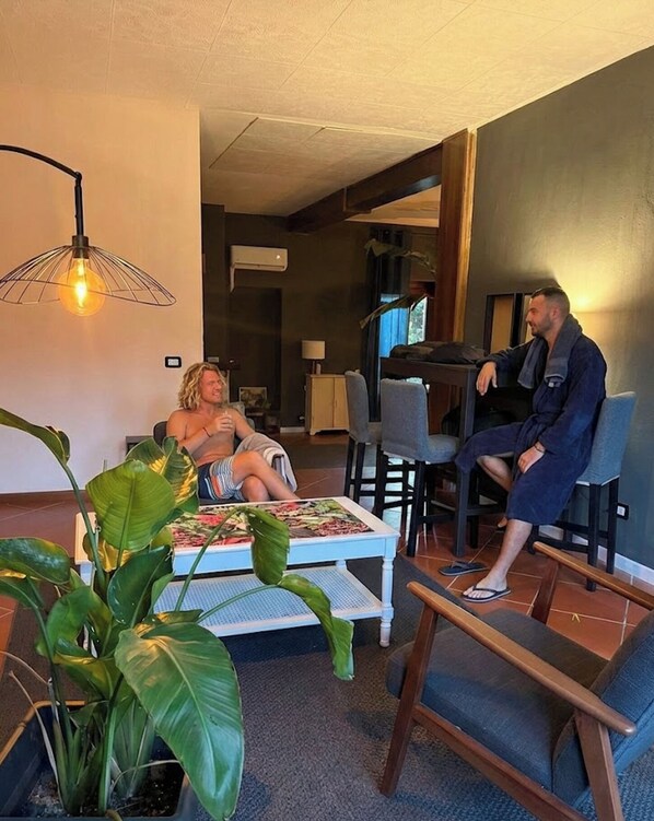 A living room with a dining area, a sofa, a coffee table, and a potted plant. - B&B RIO GRANDE (Massarosa)