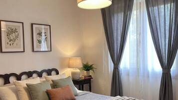 Un dormitorio con una cama, una mesita de noche con una lámpara, una planta e imprime botánicas enmarcadas en la pared.