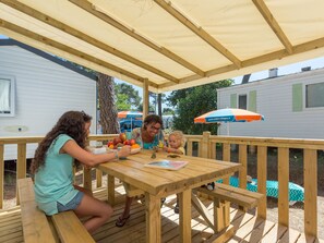 A wooden deck with a picnic table, surrounded by wooden railings and a covered area with an umbrella. - Palmyre - Confort 2 - 5p (52) (Les Mathes)