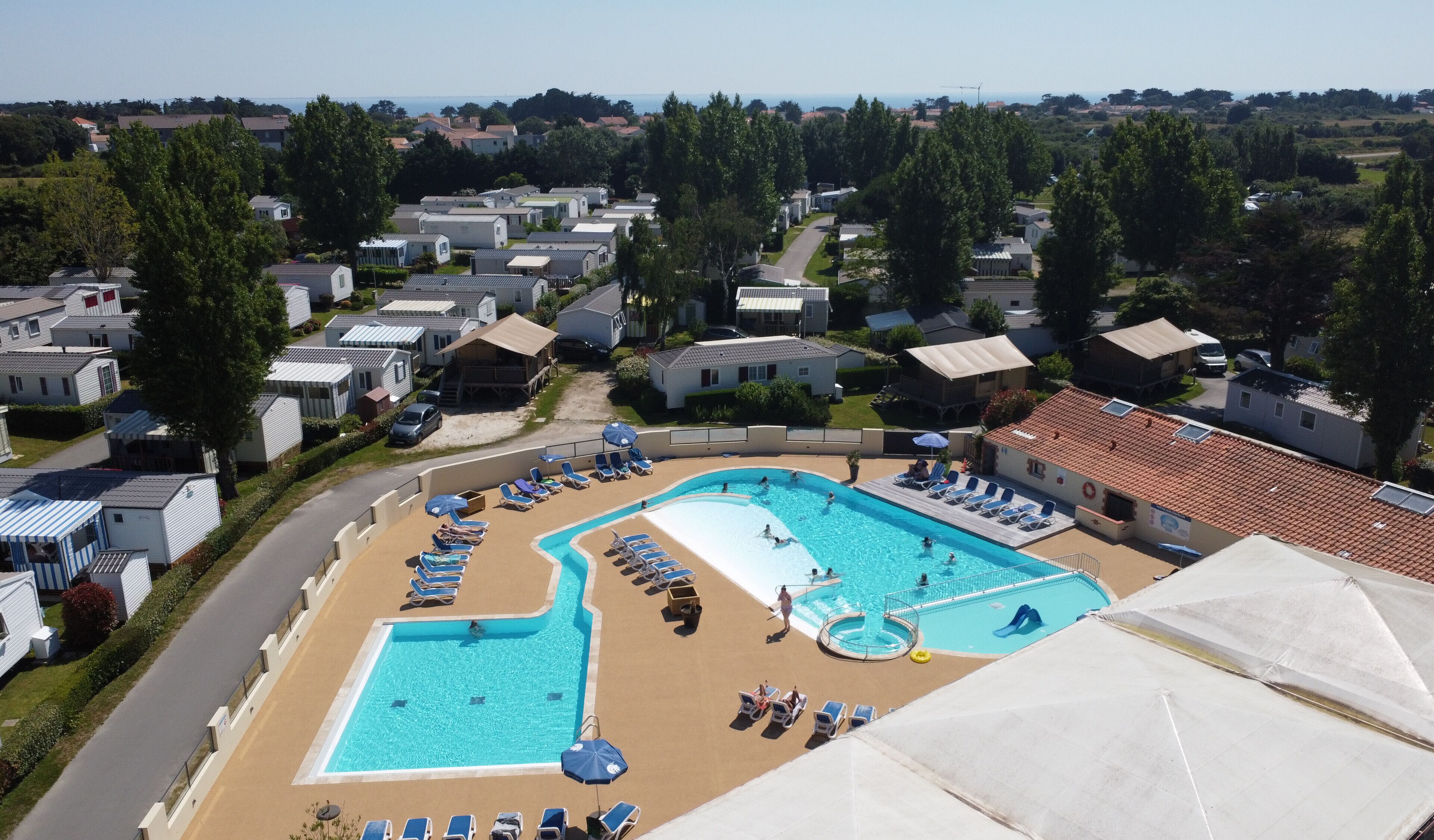 Ein großer Pool, umgeben von Liegestühlen und Sonnenschirmen, mit Blick auf eine Wohngegend im Hintergrund.