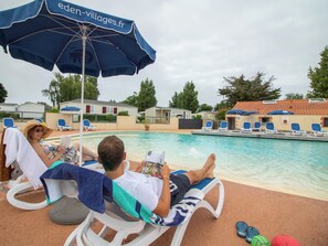 A poolside area with lounge chairs and umbrellas, a swimming pool, and a building with a tiled roof in the background. - Gildas - Privilège 4 - 8p (2) (Préfailles)