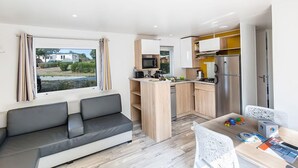 Un ambiente compatto con divano, angolo cottura, zona pranzo e vista su un quartiere residenziale.