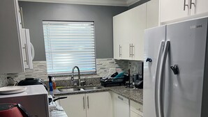 Una cocina moderna con armarios blancos, un refrigerador de acero inoxidable y una encimera de granito.