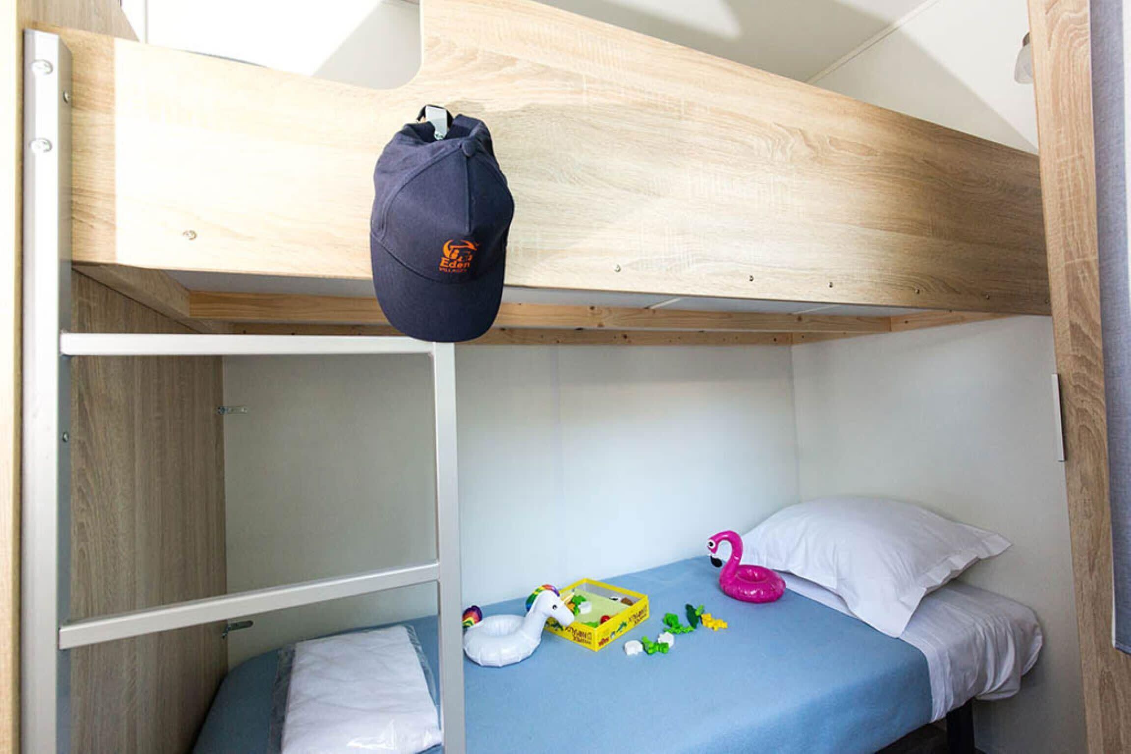 Een stapelbed met een houten hoofdbord, een opbergzak en speelgoed op het onderste bed.