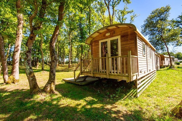 A wooden cabin with a porch, surrounded by trees. - Bréhadour - Roulotte - 4p (1) (Guérande)