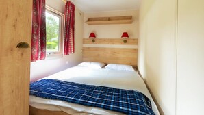 Une chambre à coucher avec un lit, une fenêtre ornée de rideaux rouges et une tête de lit en bois.
