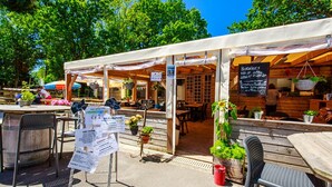 Un café en plein air avec des tables et des chaises, un tableau affichant le menu et des plantes en pot.