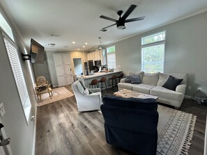 A modern living room with a sofa, armchair, and ottoman, a kitchen area with bar stools, and a ceiling fan. - If you prefer wildlife over nightlife this is the place for you, Fakahatchee! (Copeland)