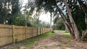 Un camí de grava al costat d'una tanca de fusta, amb arbres i vegetació al fons.