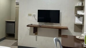 Ein Hotelzimmer mit Flachbildfernseher an der Wand, einem Holztisch mit Stuhl und einer kleinen Küchenzeile mit Kühlschrank und Spüle.