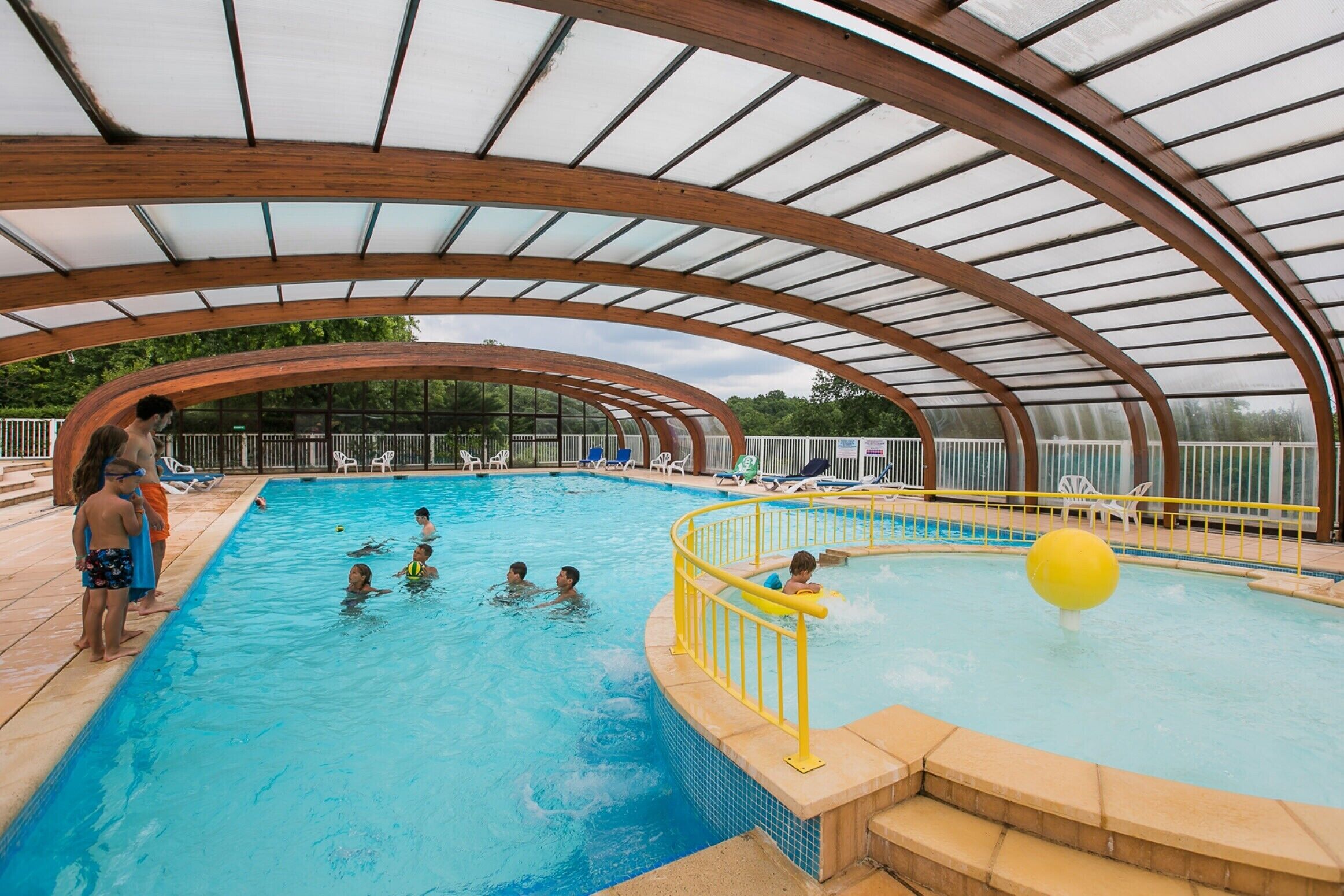 Une piscine intérieure dotée d’un toit abrité, d’une eau claire et d’une rambarde de sécurité jaune.