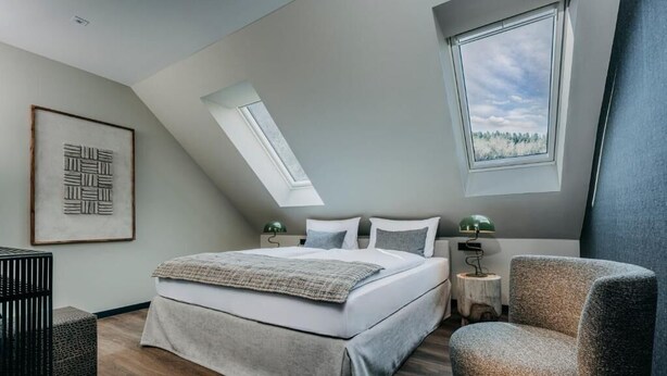 Un dormitorio moderno con una cama grande, dos mesitas de noche, una silla y un tragaluz.