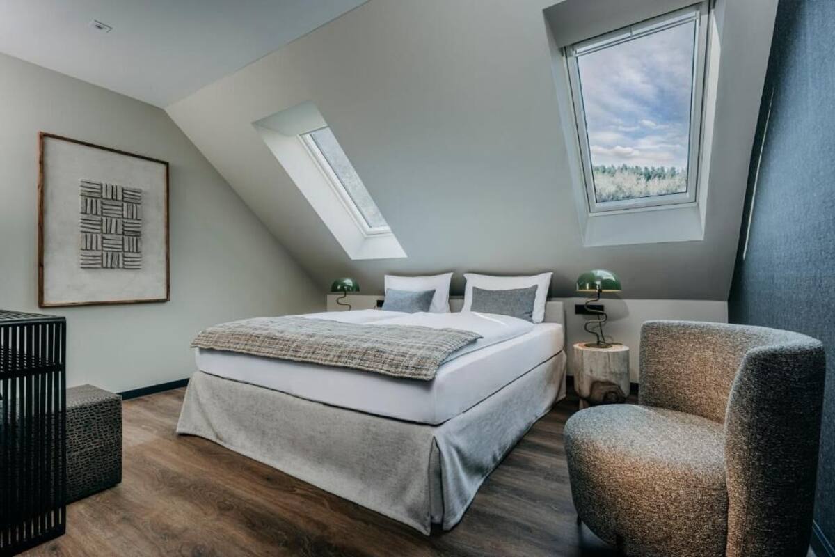 A modern bedroom with a large bed, two bedside tables, a chair, and a skylight.