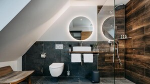Un baño moderno con tocador de madera, un espejo redondo, inodoro y zona de ducha.