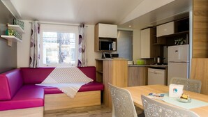 A compact living space with a red sofa, a dining table, and a kitchenette. - Bréhadour - Confort 4 TV - 9p (Guérande)