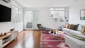 Una sala moderna con un sofá, sillas, una mesa de centro y un televisor. Hay una escalera que lleva a un espacio al aire libre.