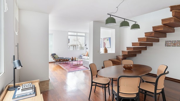 Una sala de estar moderna con una escalera de madera, un comedor con una mesa redonda y un rincón de descanso acogedor.