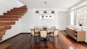 Un comedor moderno con una escalera de madera, una mesa redonda con sillas y vistas amplias a través de grandes ventanales.