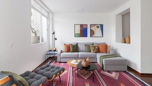 Una sala de estar moderna con un sofá gris, cojines coloridos, un tapete estampado y una mesa de centro con adornos.