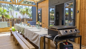 Un área de comedor al aire libre con terraza de madera, zona de estar techada y una parrilla.