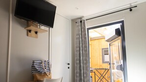 A bedroom with a TV, a desk, a chair, a bed, and a view of an outdoor wooden deck. - Palmyre - Tribu - 13p (7) (Les Mathes)