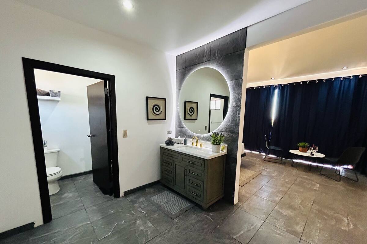Un baño moderno con tocador de tonos oscuros, un espejo grande y una zona de ducha separada con cortina.