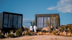 Deux bâtiments modernes aux façades en verre, avec un paysage désertique et une végétation clairsemée au premier plan.
