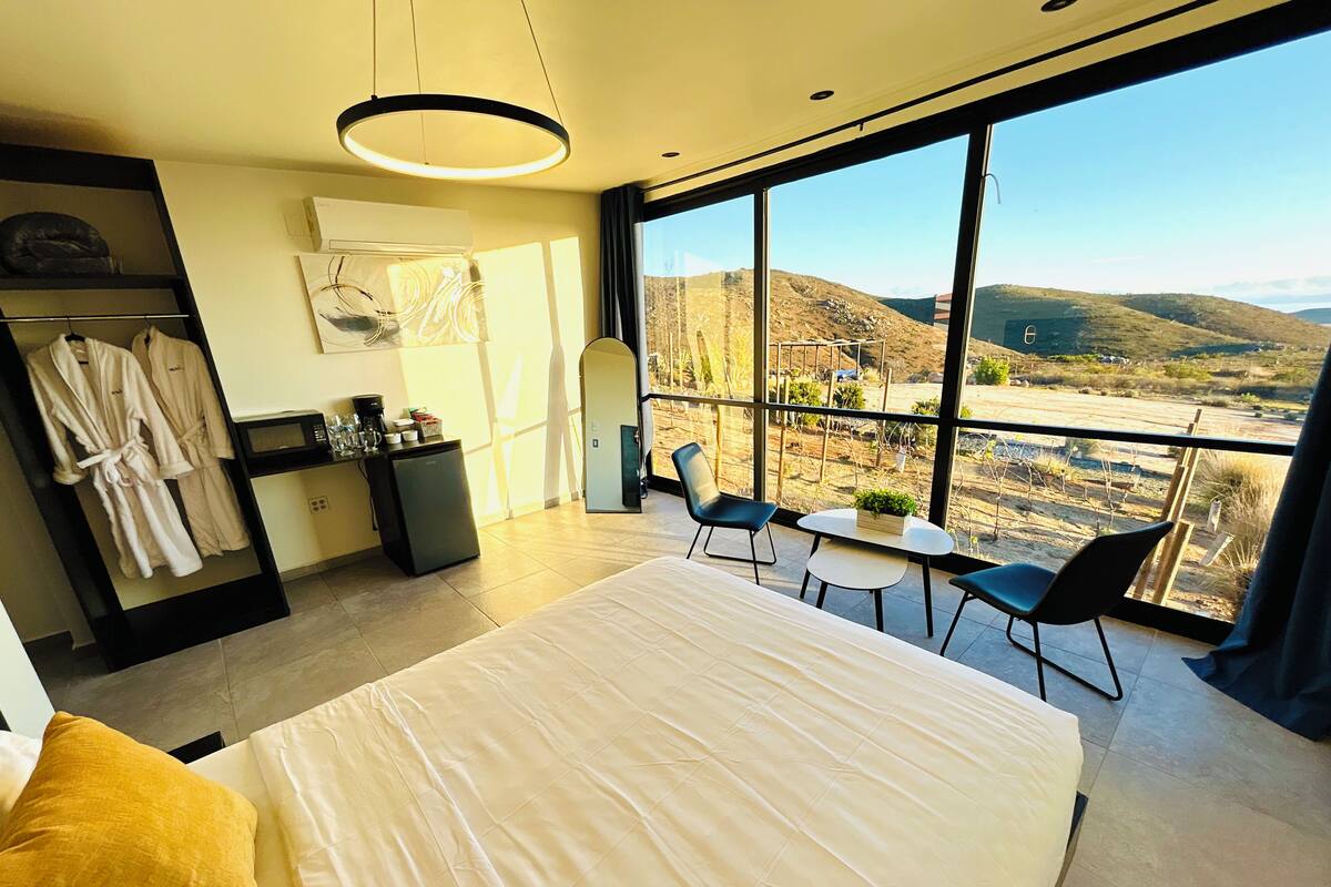 Un dormitorio moderno con una cama grande, un escritorio pequeño, una silla y vistas al campo.