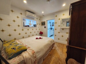A bedroom with a bed, a wooden floor, a window with curtains, a wall-mounted air conditioner, and a door leading to a bathroom. - Cozy Artistic Garden View Suite at Vancouver's Only Lake - and only 7 mins to dt (Vancouver)