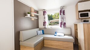 A cozy interior with a built-in bench, a microwave, and a window with curtains. - Bréhadour - Confort 2 TV - 5p (2) (Guérande)