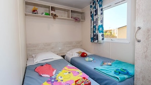 Una habitación con dos camas, una ventana con cortinas, un estante con juguetes y una caja de cartas de UNO.