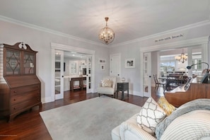 A spacious living room with a large wooden dresser, a chandelier, and a cozy seating area with patterned cushions.