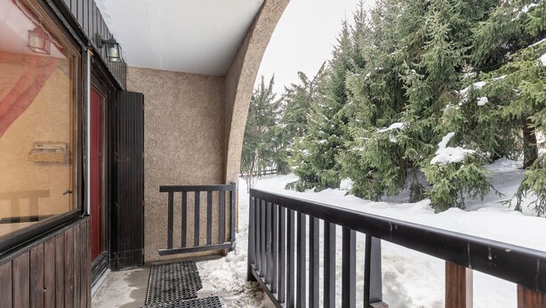 Ein mit Schnee bedeckter Balkon mit Holzwand, einem Metalltritt und Blick auf schneebedeckte Bäume.