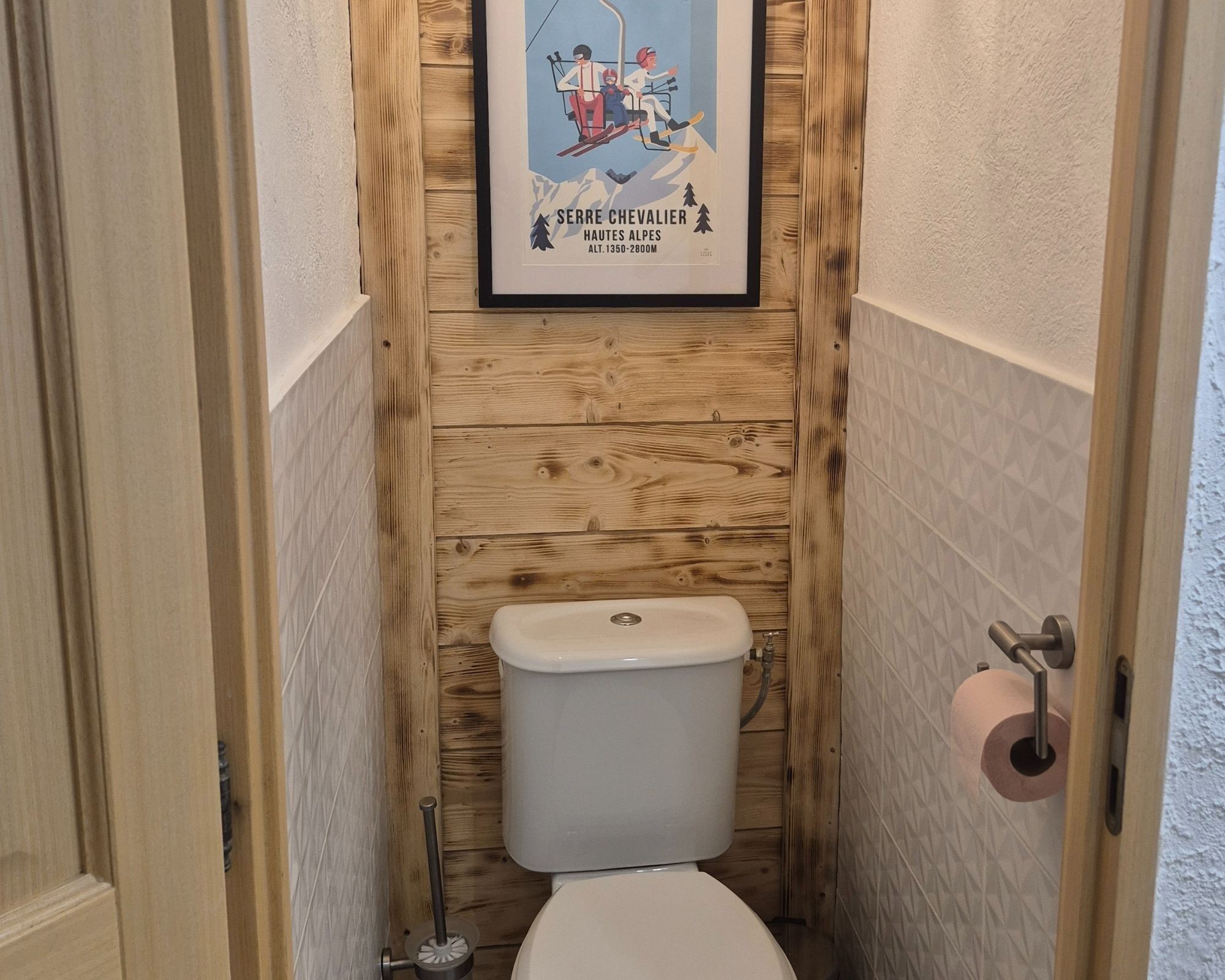 A small, wooden-paneled bathroom with a toilet, a hand dryer, and a poster of a ski lift.